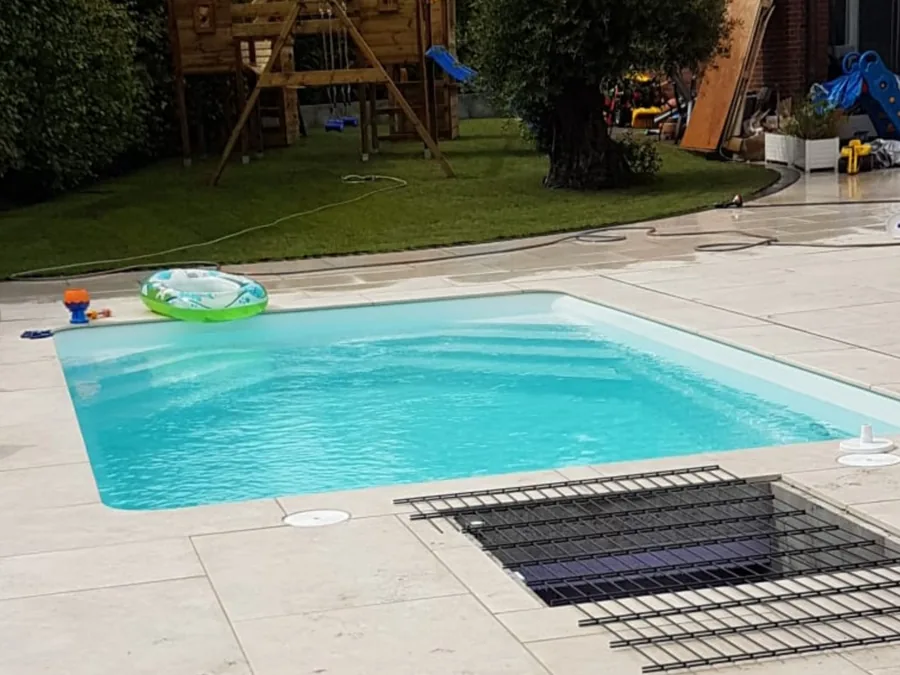 Schwimmbecken mit umlaufender Plattenfläche und angrenzendem Rasen